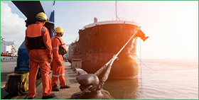 Coface: United States Country Risk Focus. The photo shows two men in high viz protective equipment standing by a ship in a harbour.